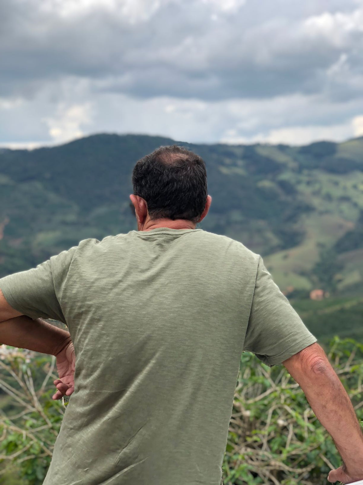 Man seen from behind standing with hands on hips, overlooking green hills near Furnas, Brazil