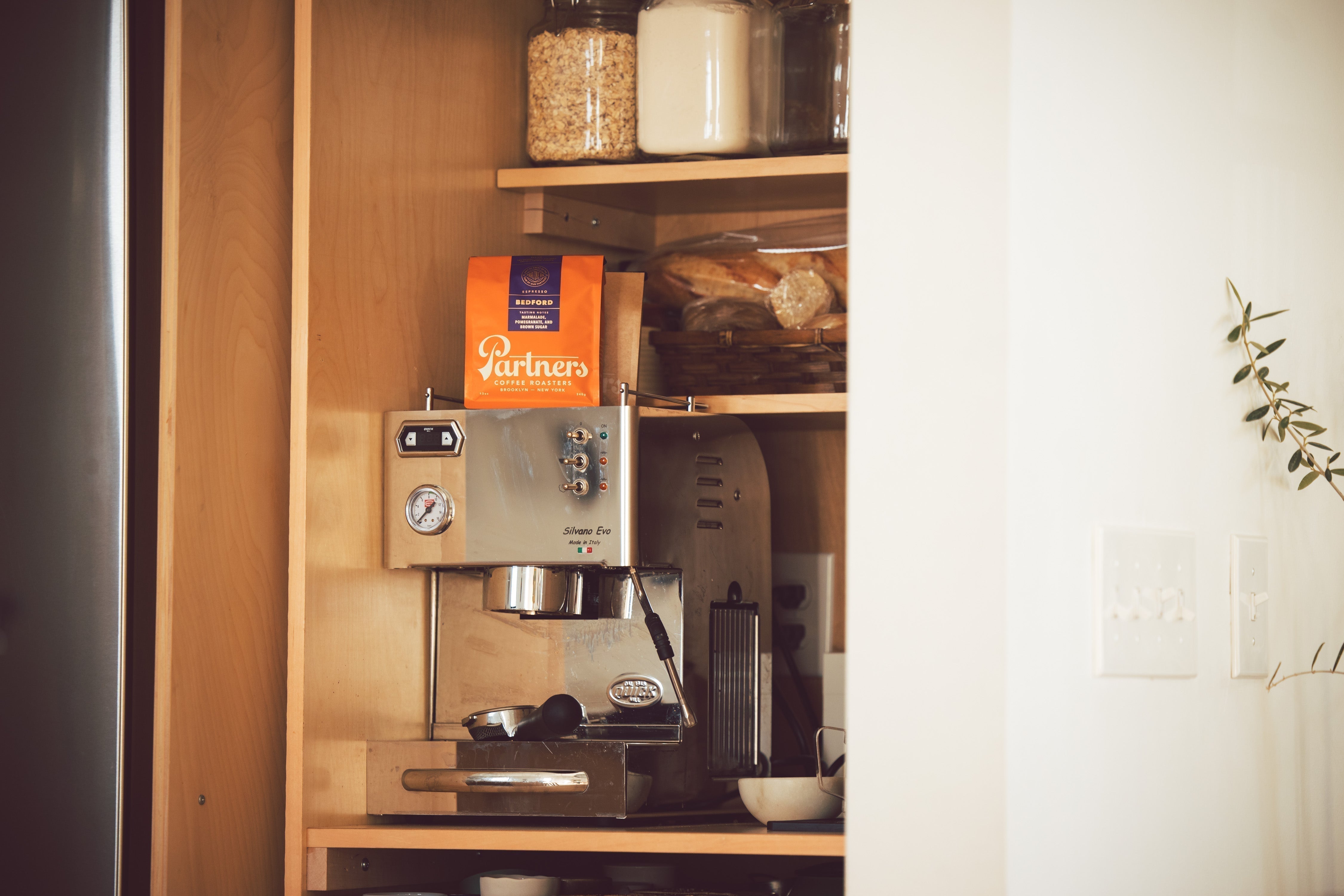 Bag of Partners Bedford coffee resting on a stainless-steel home espresso machine inside a wooden kitchen cabinet
