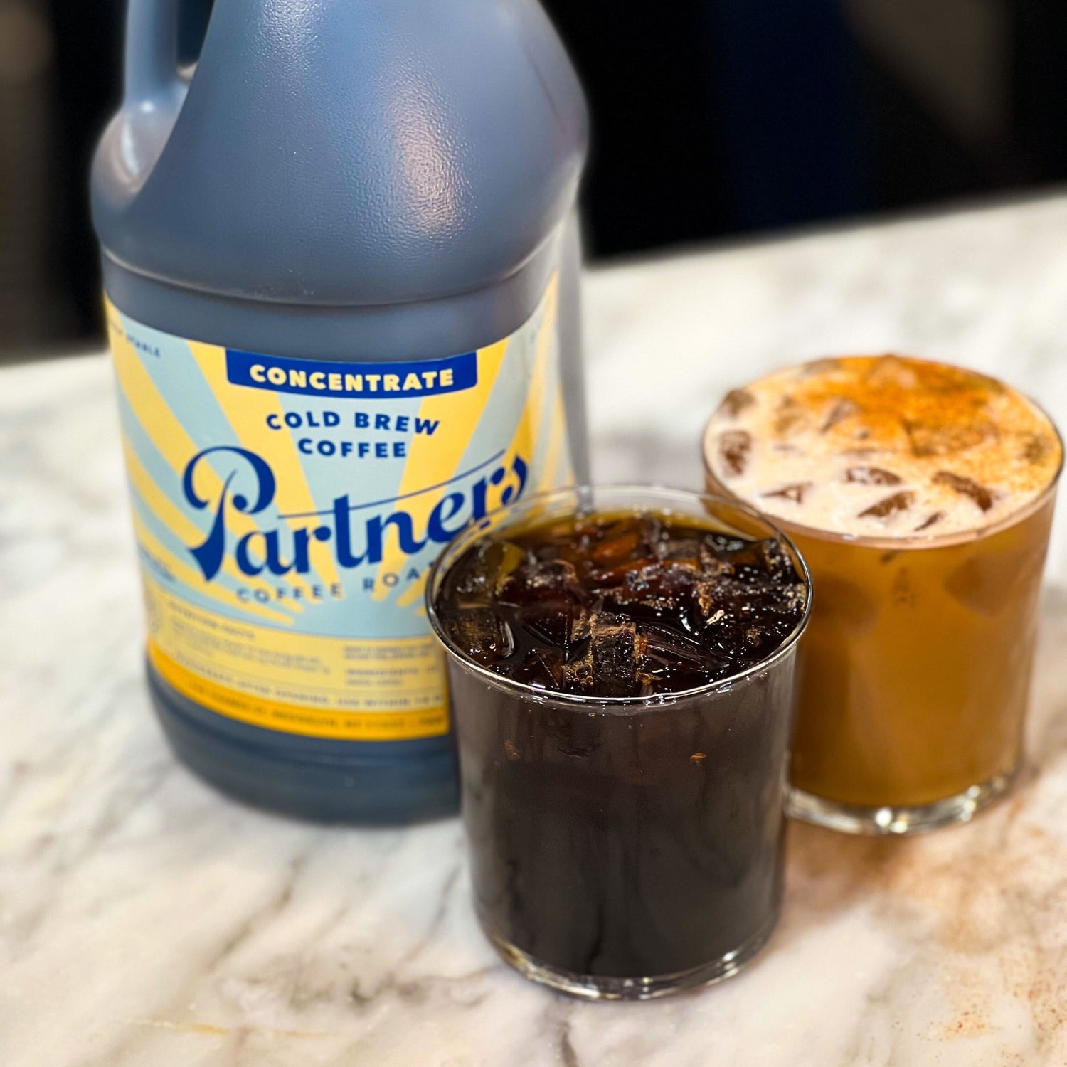 Partners Coffee image for The Mega Jug: Q&A blog post. This image depicts a 64 ounce jug of cold brew concentrate next to two different prepared beverages