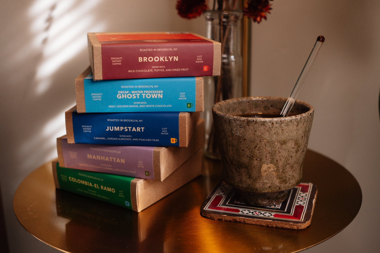 Image for What Makes Instant Coffee "Specialty" blog post. This image depicts 5 boxes of Partners Specialty Instant Coffee stacked on their sides next to a freshly brewed cup of instant coffee