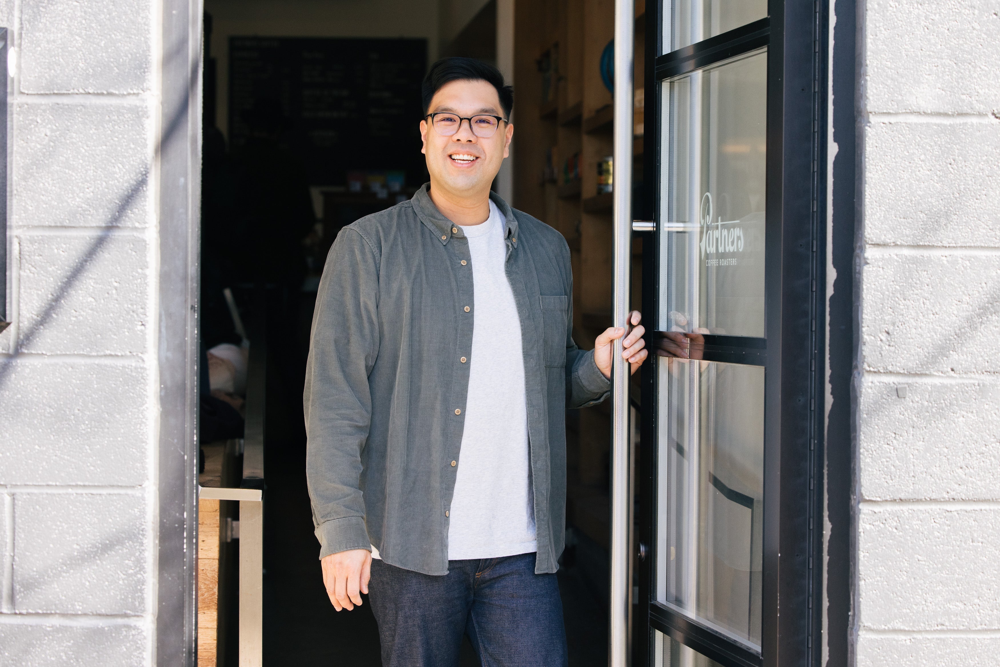 Partners Coffee Meet The Crew - Cary W. blog post. This image depicts Partners Coffee's Director of Coffee, Cary, holding open the door to the Partners Coffee storefront in Williamsburg