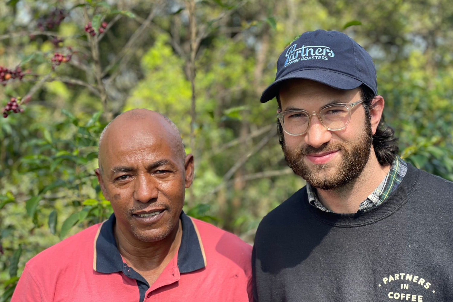 Partners Coffee Ethiopia - Suke Quto blog post. This image depicts producer Tesfaye Bekele and Partners Coffee Green Coffee Buyer, Sam, in front of trees on the Suke Quto farm.
