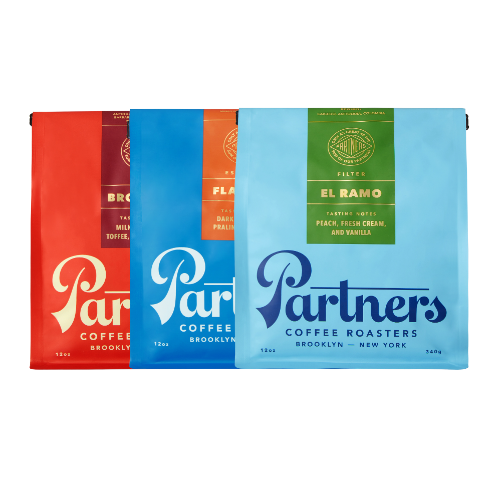 Three bags of coffee from Partners Coffee Roasters, featuring the Brooklyn Blend, Flatiron Blend, and Colombia - El Ramo. Each bag is color-coded: red, blue, and green, with white text displaying the product names.