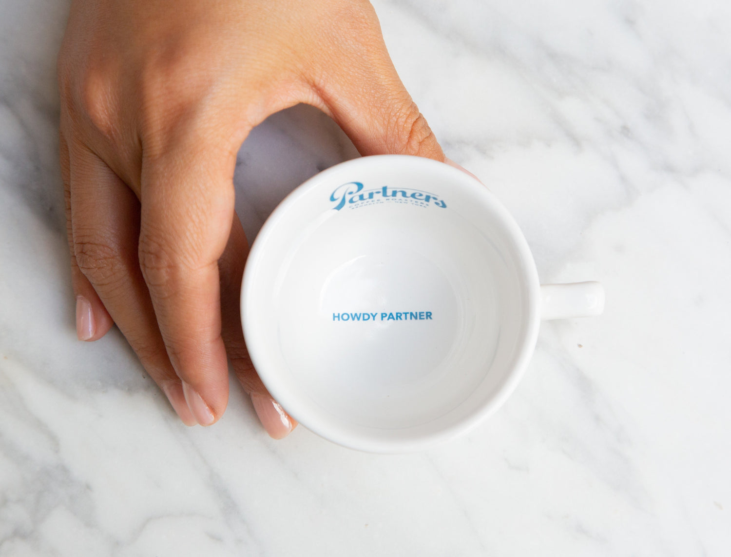Partners Coffee National Coffee Day blog post. This image depicts a hand cupped around a Partners Coffee espresso cup with the message "Howdy Partner" detailed on the interior of the cup.