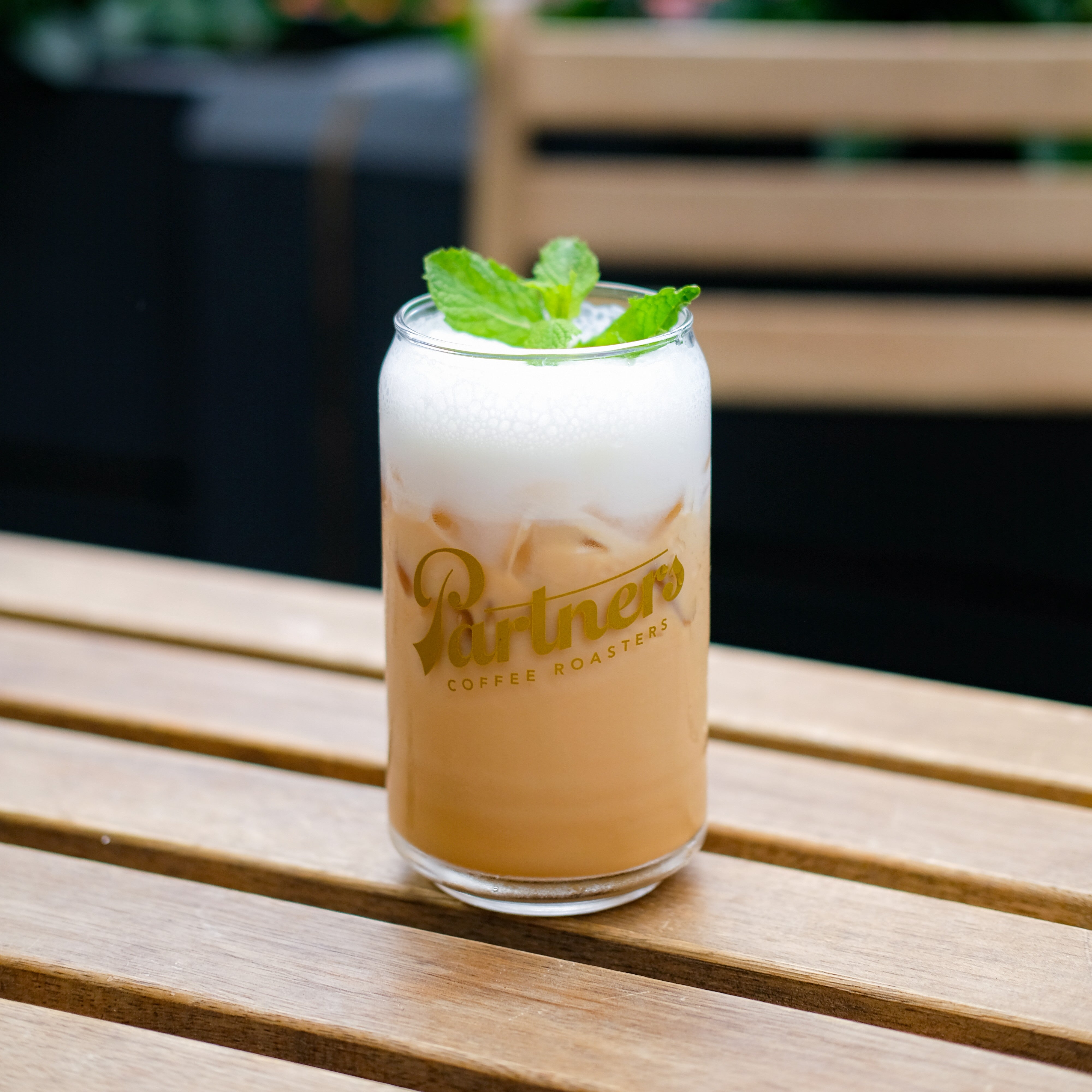 Close up view of iced Espresso Julep with frothy foam and mint in a Partners Coffee Roasters glass on a wooden table