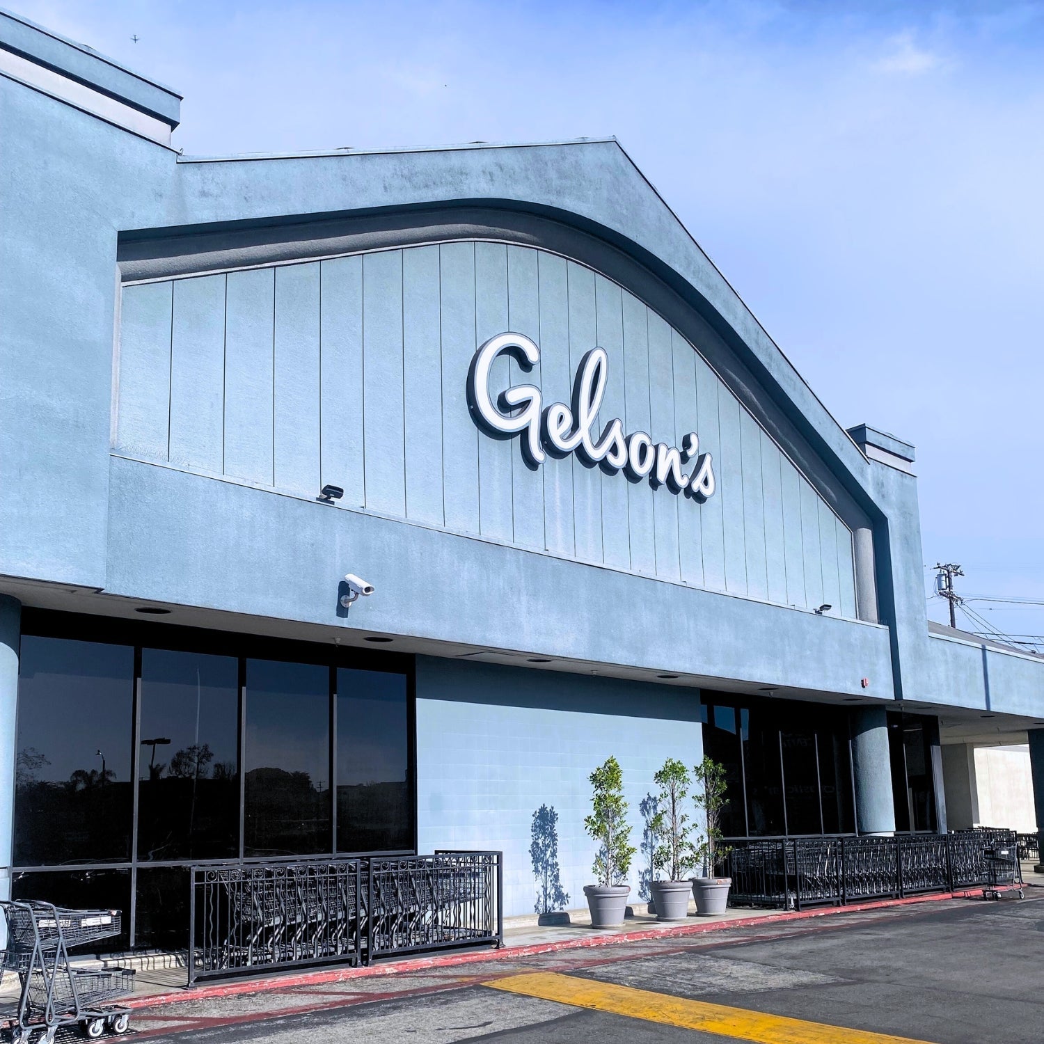 Exterior of Gelson’s Market storefront with pale blue façade, large Gelson’s sign, shopping cart corrals and potted plants by the entrance