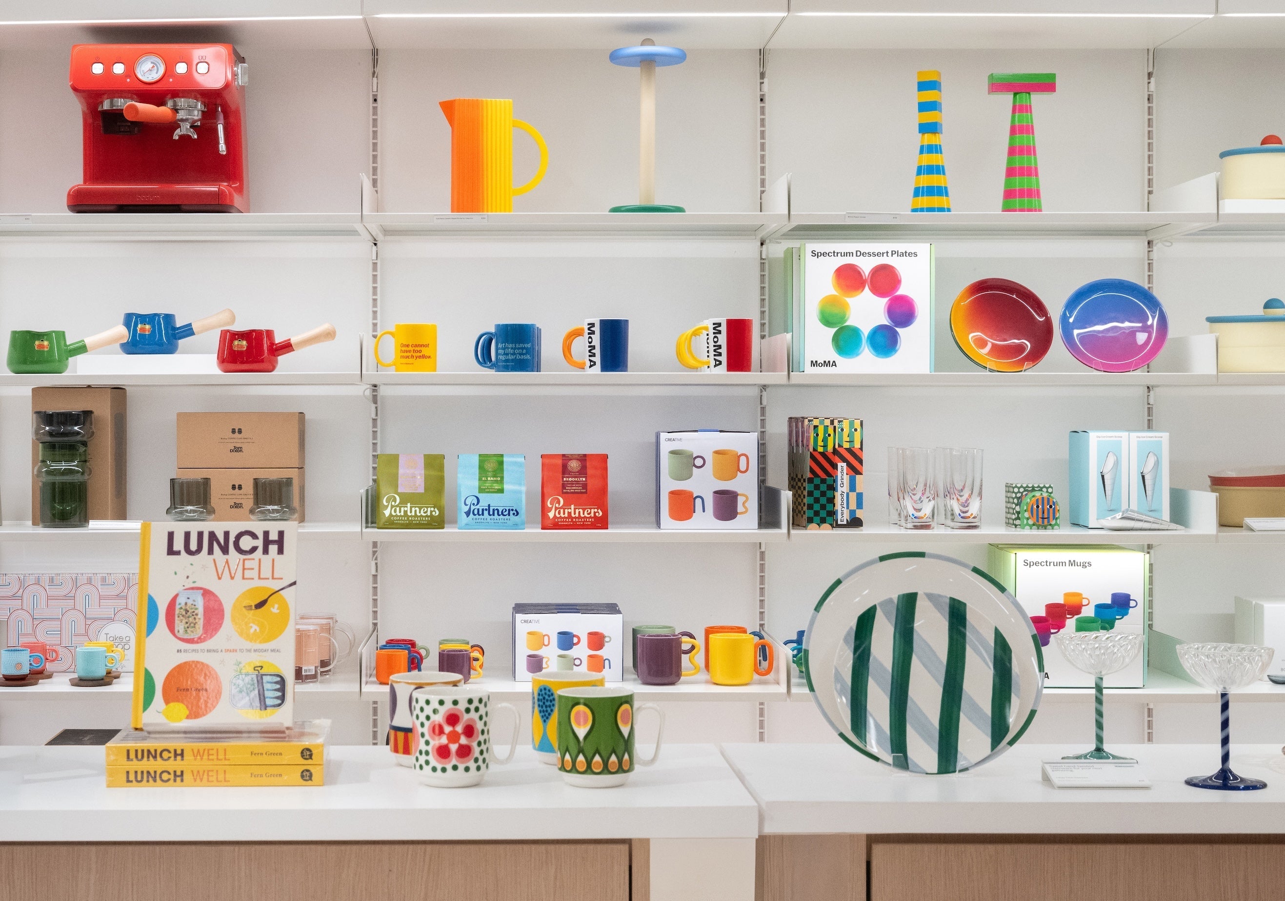 MoMA Design Store shelf display with colorful mugs, plates, and Partners Coffee bags on white shelves