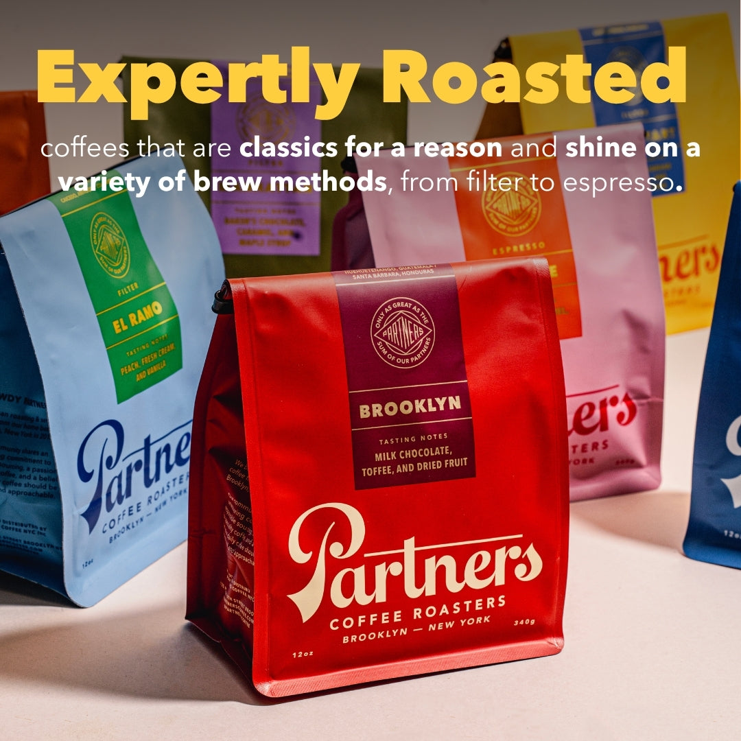 Three-quarter front of Mainstay Shuffle bag with headline Expertly Roasted and red Partners Brooklyn bag in blurred group