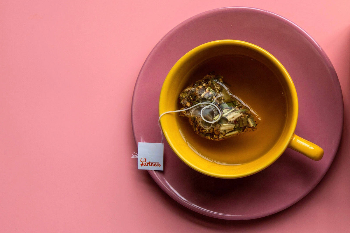 Overhead view of turmeric ginger tea steeping in a yellow cup on a mauve saucer against a pink background